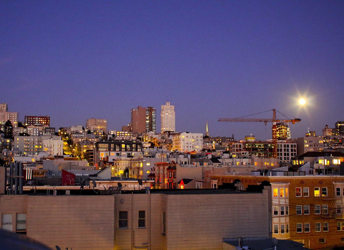 About Our Agency - Aerial View of Many Buildings on a Slant With a Construction Crane and a Very Bright Moon in the Background